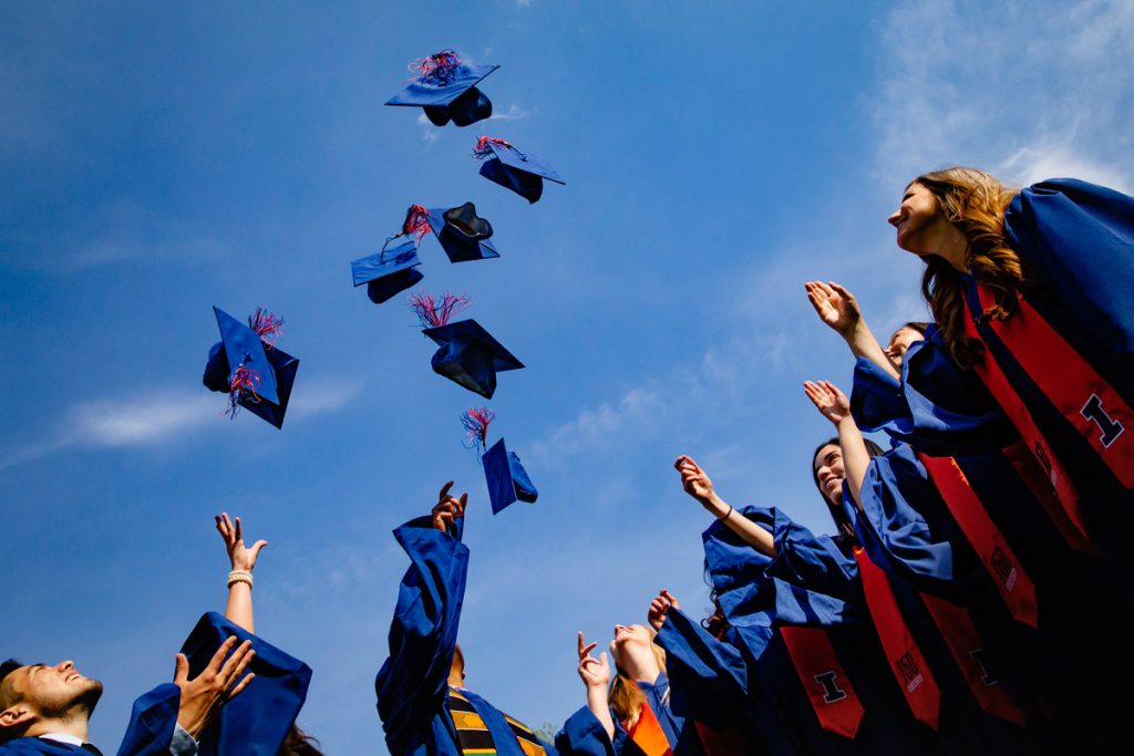 Female and male graduates in gowns tossing caps into the air.